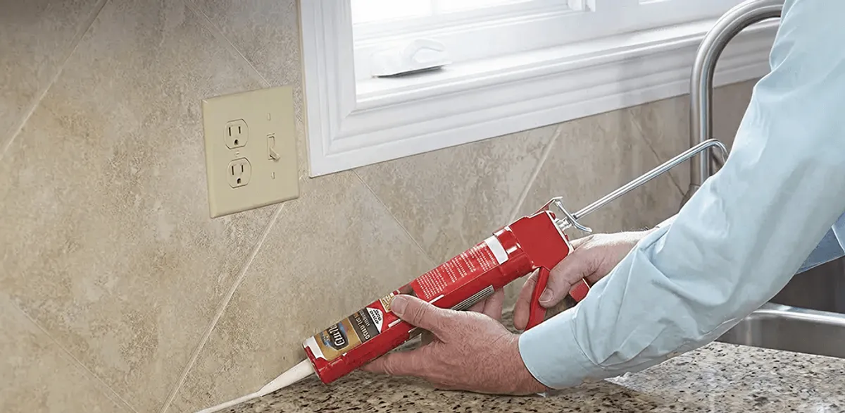 Handyman applying caulk along a kitchen backsplash and countertop seam in Louisville, KY