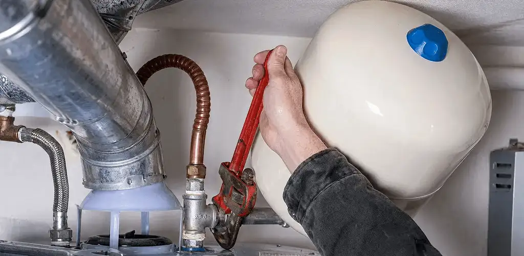 Water heater repair technician tightening plumbing connections near a tank unit in Louisville, KY